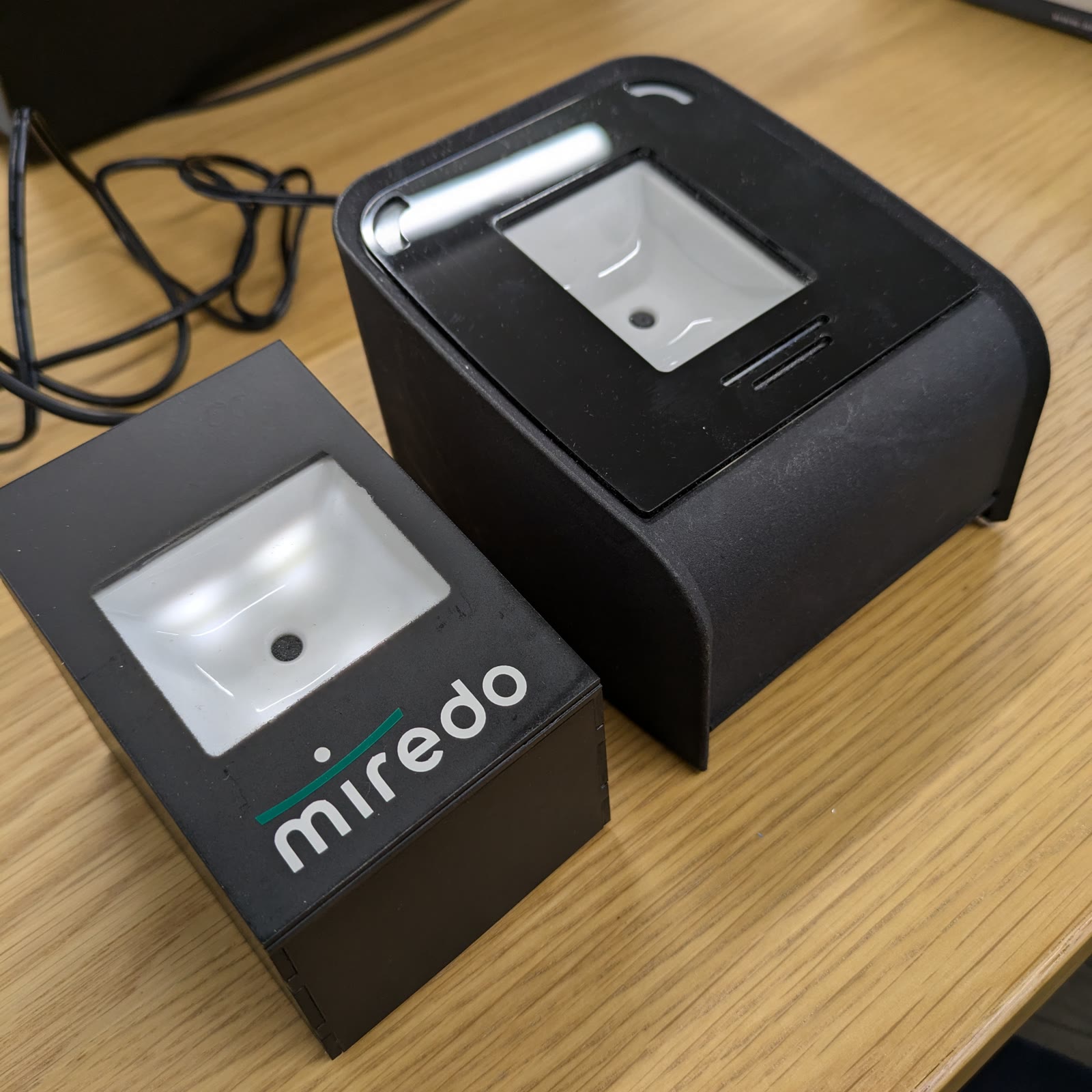 miredoロゴ入りQRリーダー端末の実機2台。黒い筐体に読み取り窓を備えたデザイン